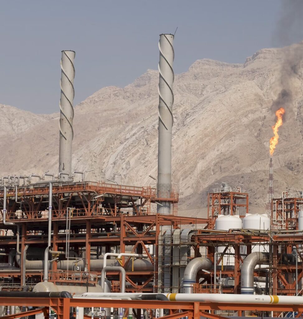 An Iranian oil and gas complex burns off gas against a desert mountain backdrop.